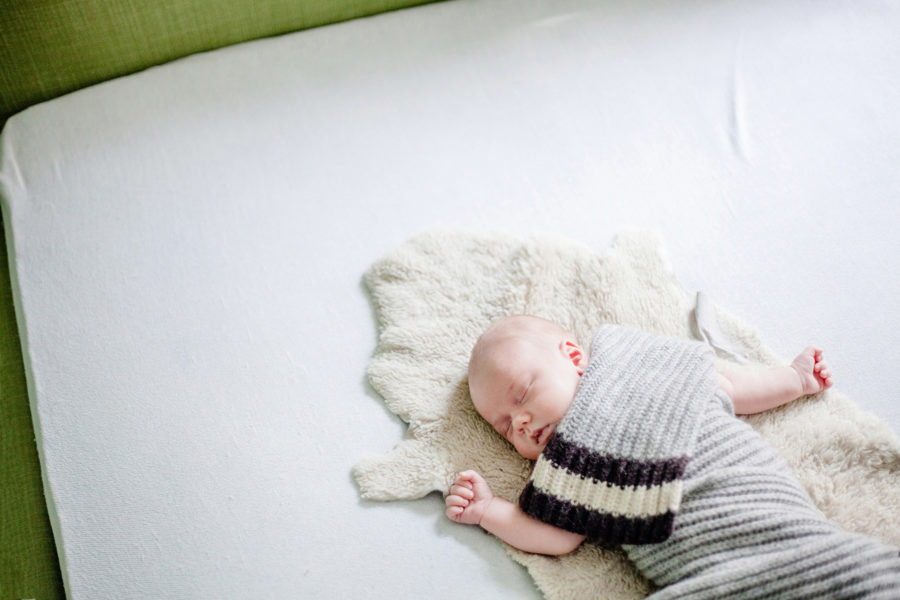 Baby liegt schlafend, von einem Schal bedeckt, auf einem Lammfell im Bett seiner Eltern