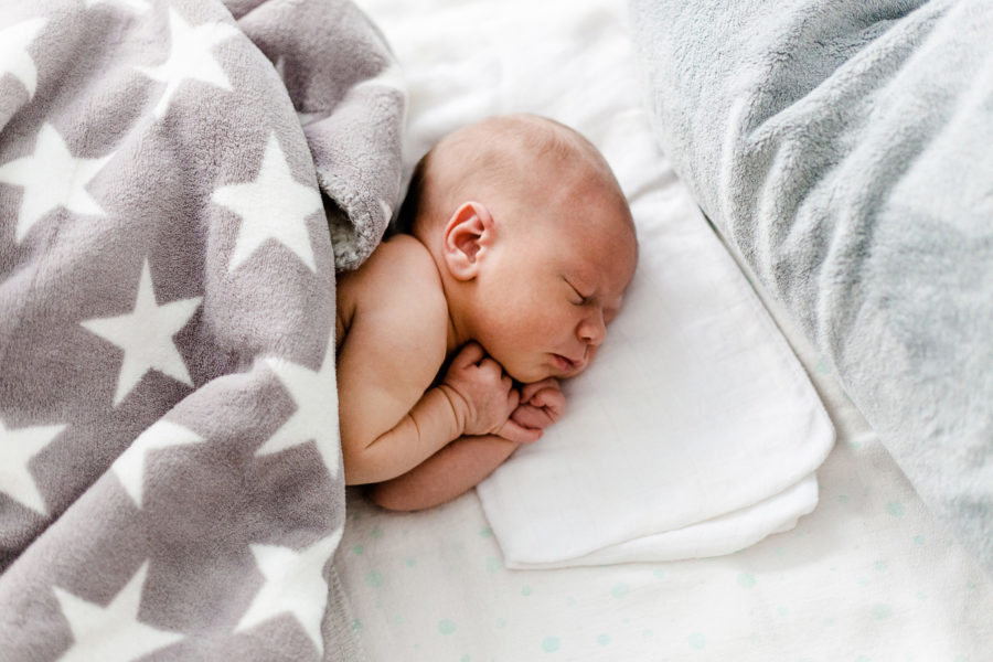 Baby liegt schlafend im Bett umgeben von weichen Decken und Kissen