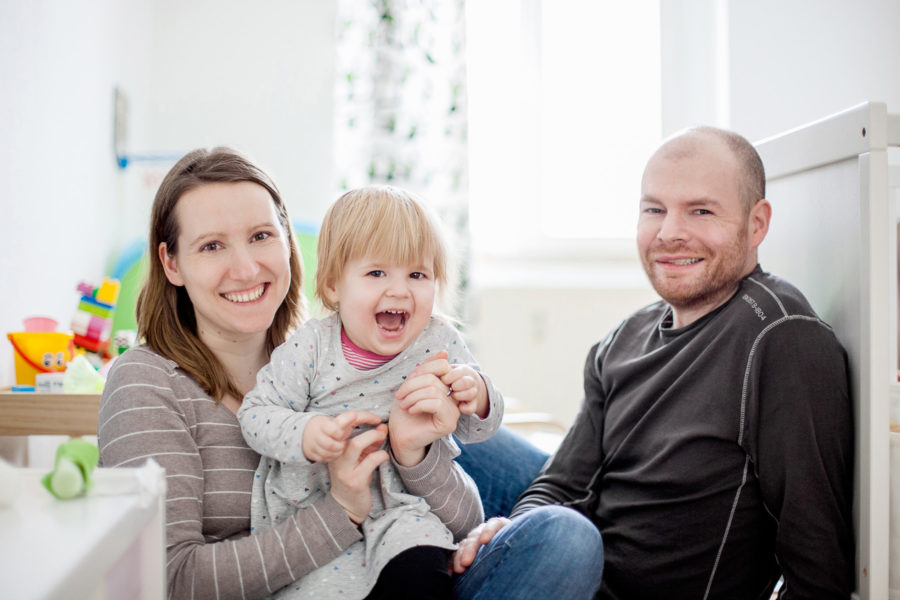 glückliche Familie mit Kleinkind sitzt lachend im Kinderzimmer