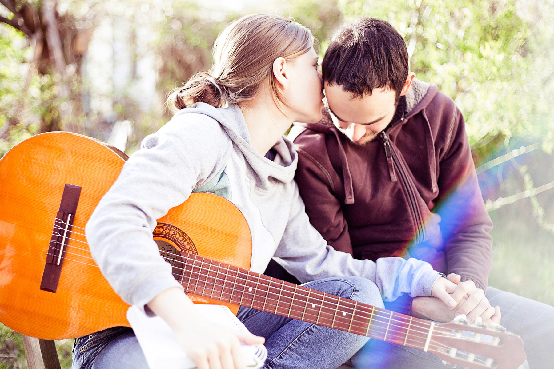 junge Frau mit Gitarre, hält die Hand ihres Freundes und flüstert ihm ins Ohr