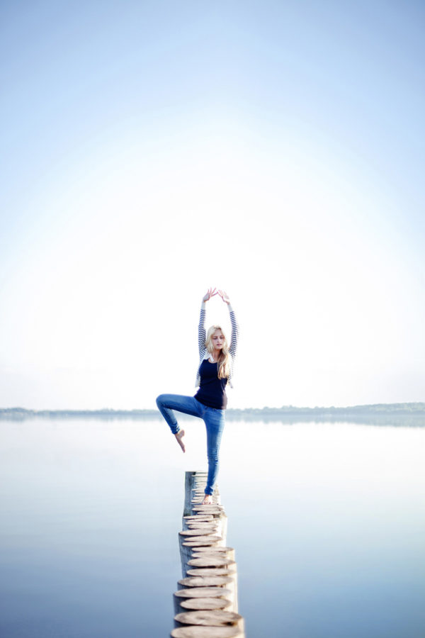 junge Frau steht in Yoga-Pose am See